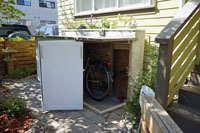 A view of the bike shed opened, showing the bicycle stored inside.  The main door is articulated to wrap around the corner doorway and fold out of the way when opened.