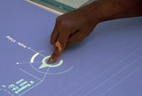 A user demonstrates a projecter-based interactive tabletop.  Image by Nick Statt via Verge.